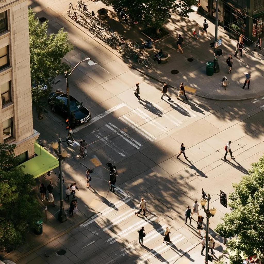 Shoppers crossing a busy city intersection lined with stores and cafes